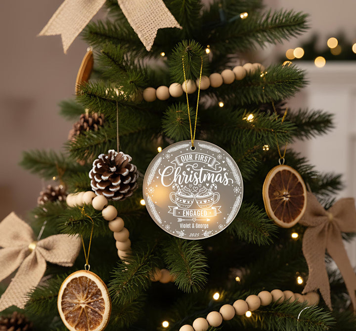 A Christmas tree decorated with ornaments, including a round ornament with the text &quot;OUR FIRST CHRISTMAS&quot; and a smaller ornament shaped like a pine cone.
