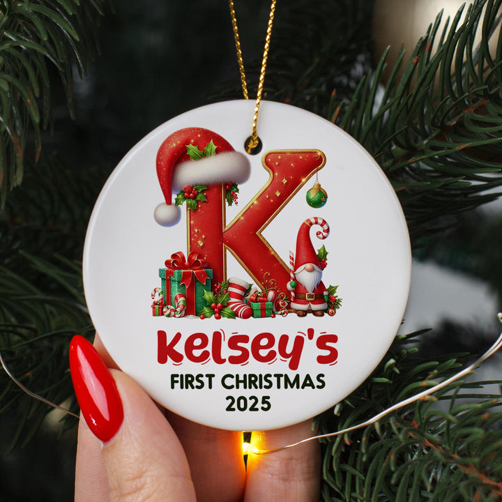A person&#39;s hand holding a white ornament with a red letter &quot;K&quot; and a gnome, along with various Christmas-themed decorations.