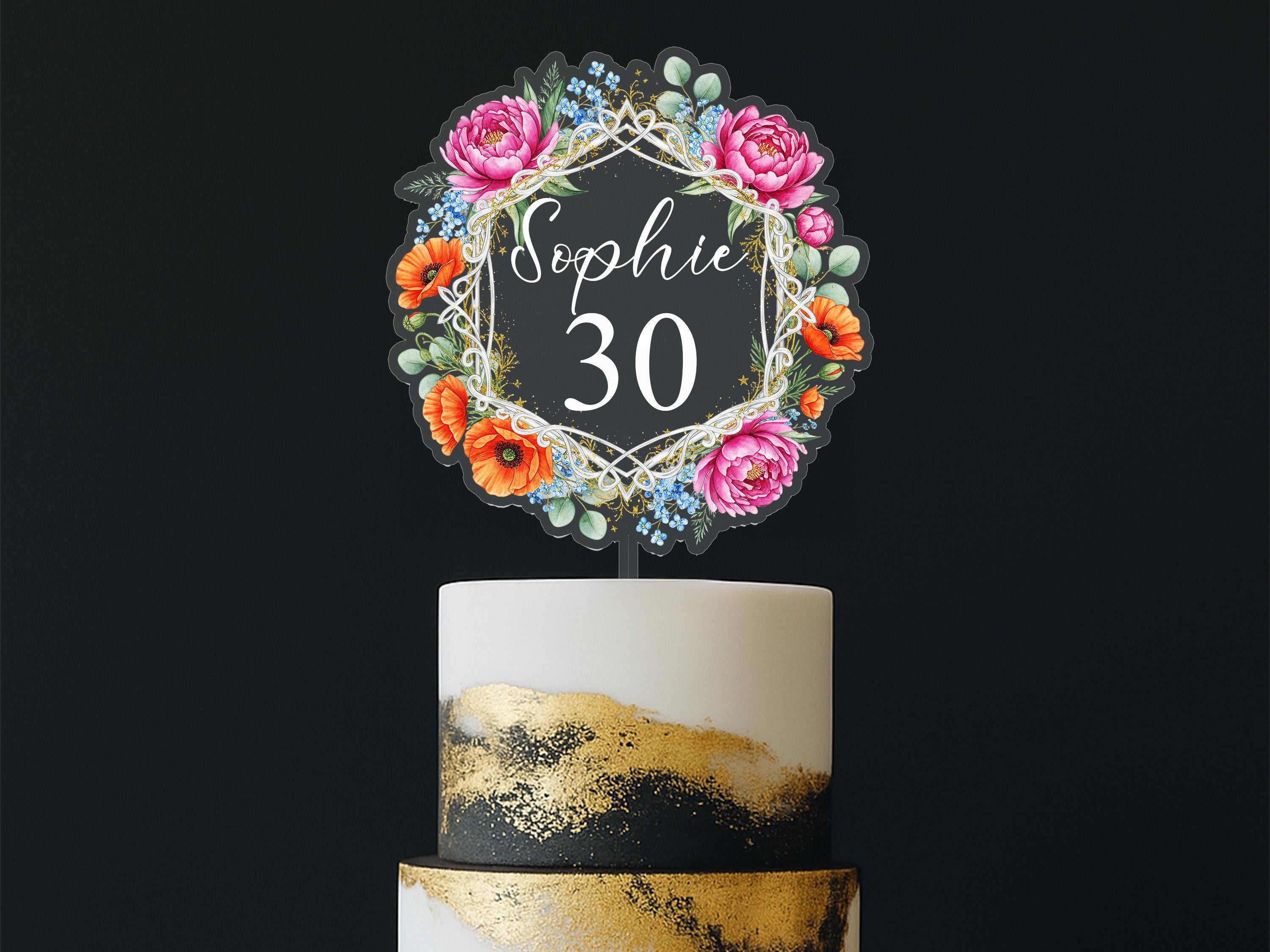A cake topper with a floral design and the name "Sophie" written on it, placed on top of a two-tiered cake.