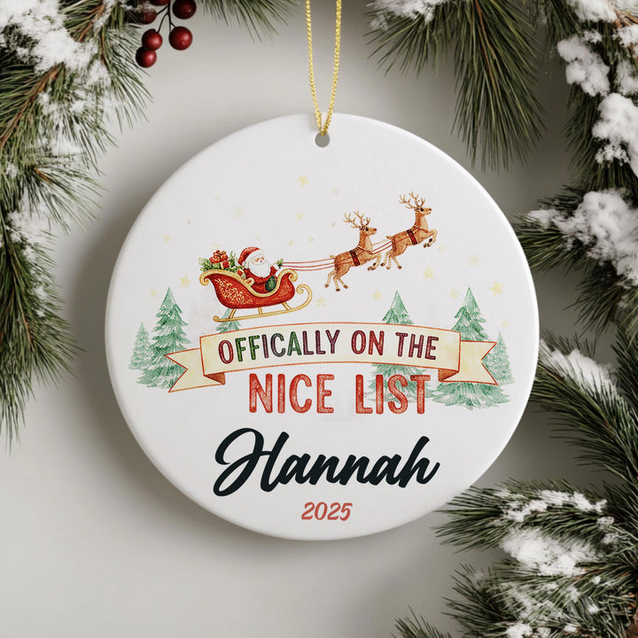 A white ornament with a Santa Claus sleigh and reindeer, along with the text &quot; Officially on the NICE LIST Hannah 2020&quot;.
