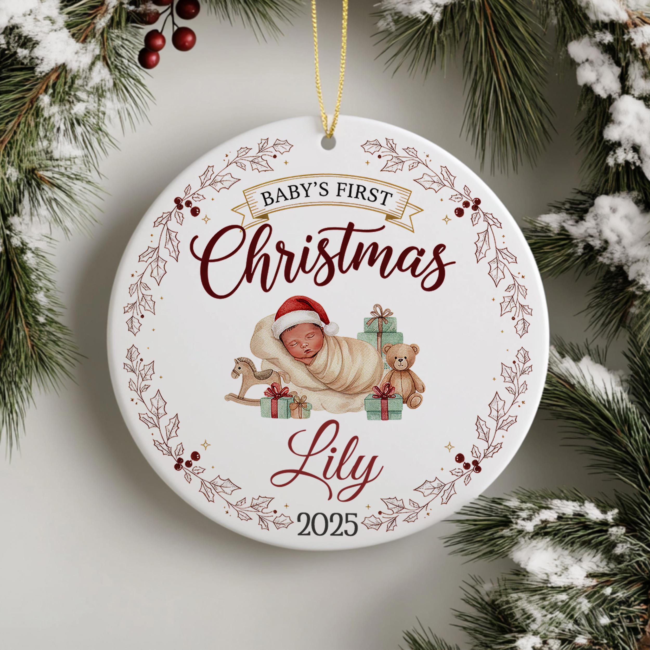 A white Christmas ornament with a baby swaddled in a blanket and a teddy bear, surrounded by holly leaves and berries. The ornament has a banner that reads "Baby's First Christmas" and "Lily" written on it.