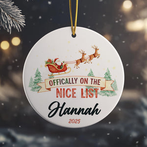 A white ornament with a Santa Claus sleigh and reindeer, along with the text " Officially on the NICE LIST Hannah" and the year "2025".