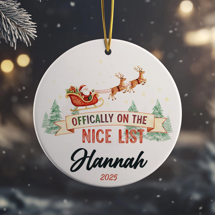 A white ornament with a Santa Claus sleigh and reindeer, along with the text &quot; Officially on the NICE LIST Hannah&quot; and the year &quot;2025&quot;.