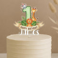 Personalised safari first birthday cake topper featuring green polka dot number 1 with cute jungle animals elephant, giraffe, lion, tropical leaves and custom name James on white celebration cake