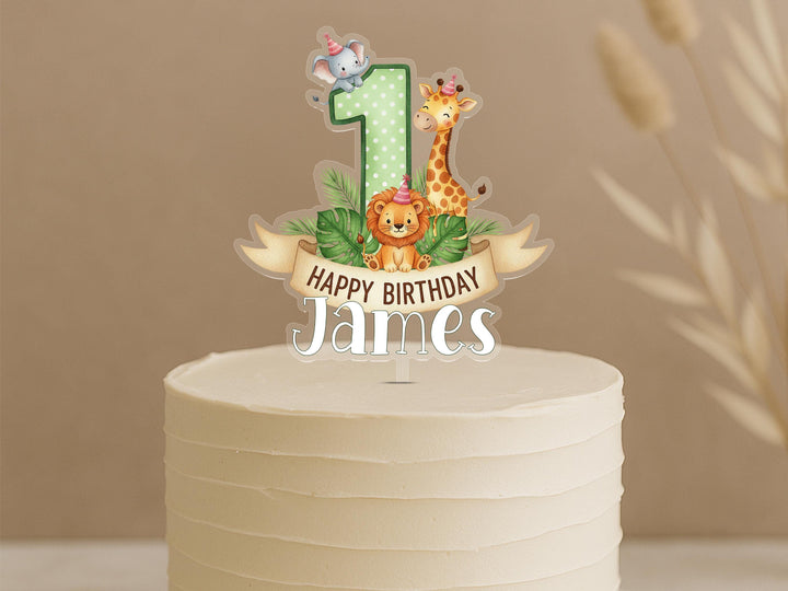 Personalised safari first birthday cake topper featuring green polka dot number 1 with cute jungle animals elephant, giraffe, lion, tropical leaves and custom name James on white celebration cake