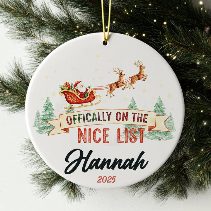 A white ornament with a Santa Claus sleigh and reindeer, along with the text &quot; Officially on the NICE LIST Hannah 2020&quot;.