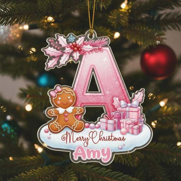 A pink glittery letter &quot;A&quot; ornament with a gingerbread man and presents, hanging on a Christmas tree.