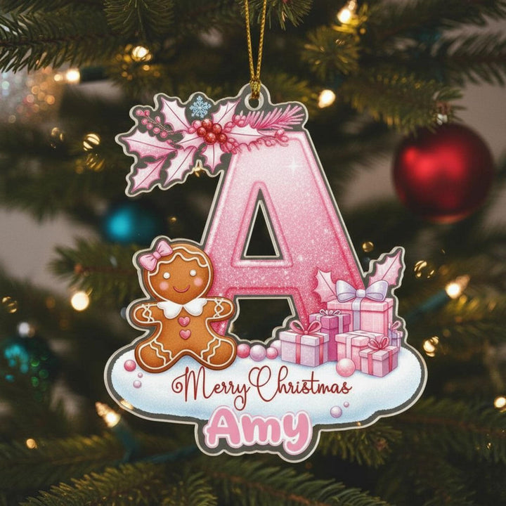 A pink glittery letter &quot;A&quot; ornament with a gingerbread man and presents, hanging on a Christmas tree.