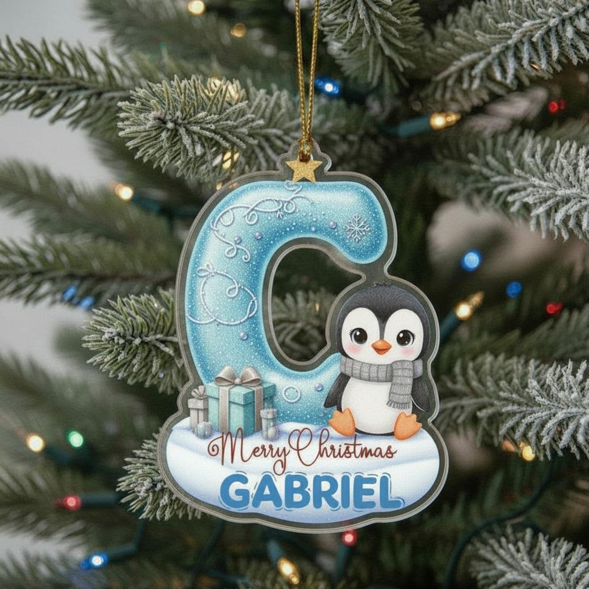 A Christmas ornament shaped like the letter "C" with a penguin design, and the name "GABRIEL" written below it.