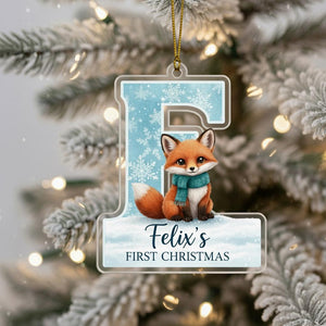 A clear ornament shaped like the letter "E" with a cartoon fox sitting on top of a snowy background, hanging on a Christmas tree.