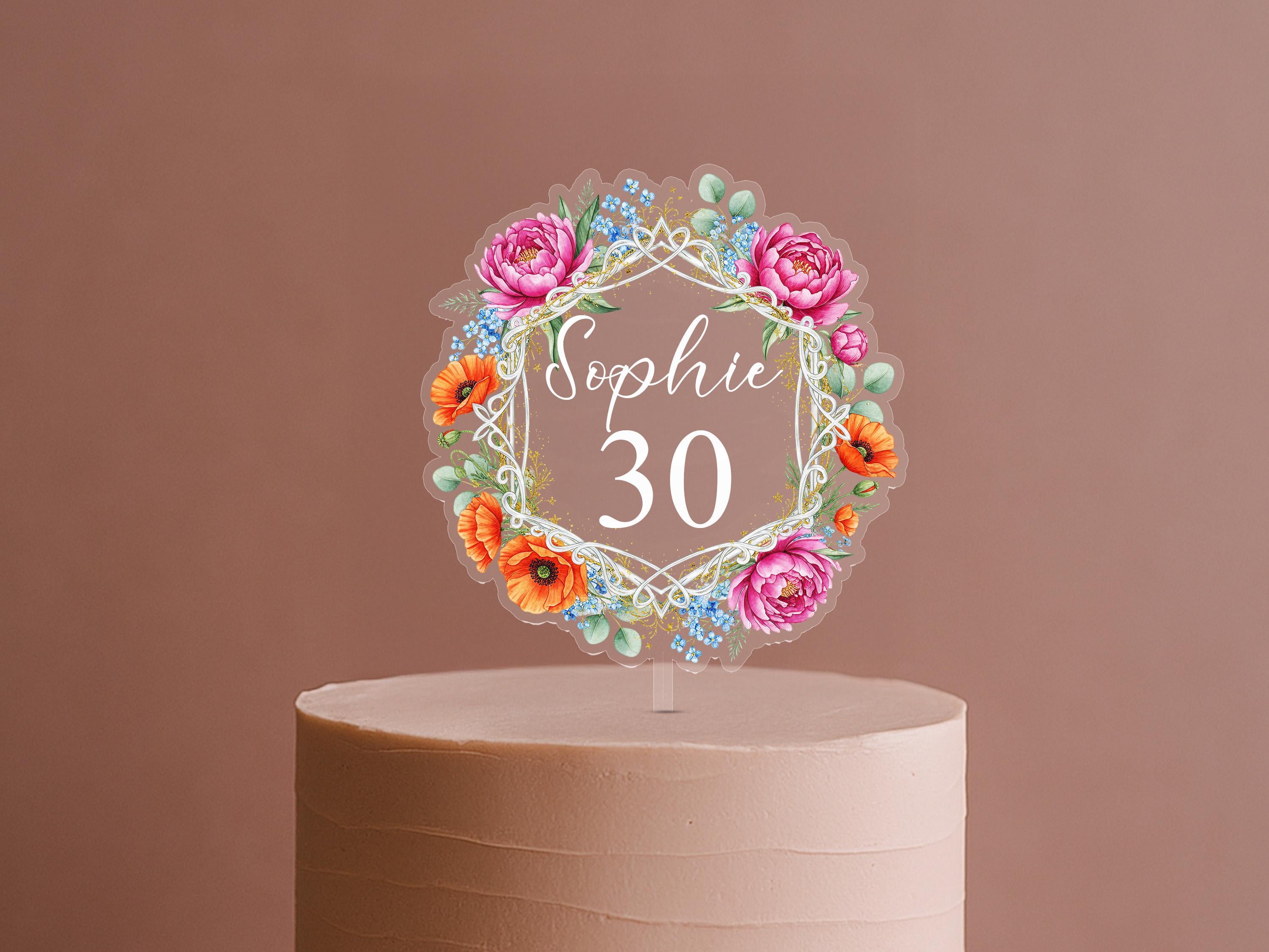 A cake topper with a floral design and the name "Sophie" written on it.