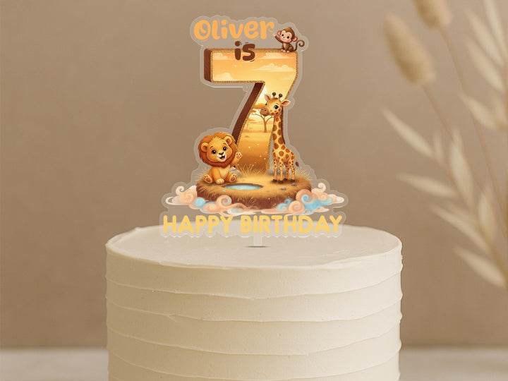 Personalised safari birthday cake topper featuring number 7 with lion, giraffe and monkey on golden sunset savanna scene, custom name Oliver, displayed on white frosted cake