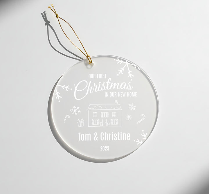 A clear glass ornament with a white design and text, hanging on a white background.