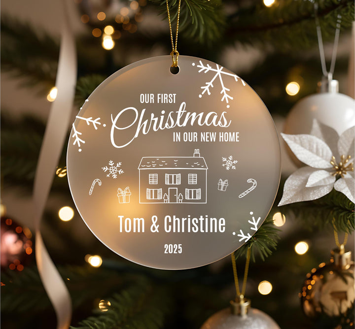 A Christmas ornament hanging on a tree, with the text &quot;Our first Christmas in our new home&quot; and the names &quot;Tom & Christine&quot; below it.