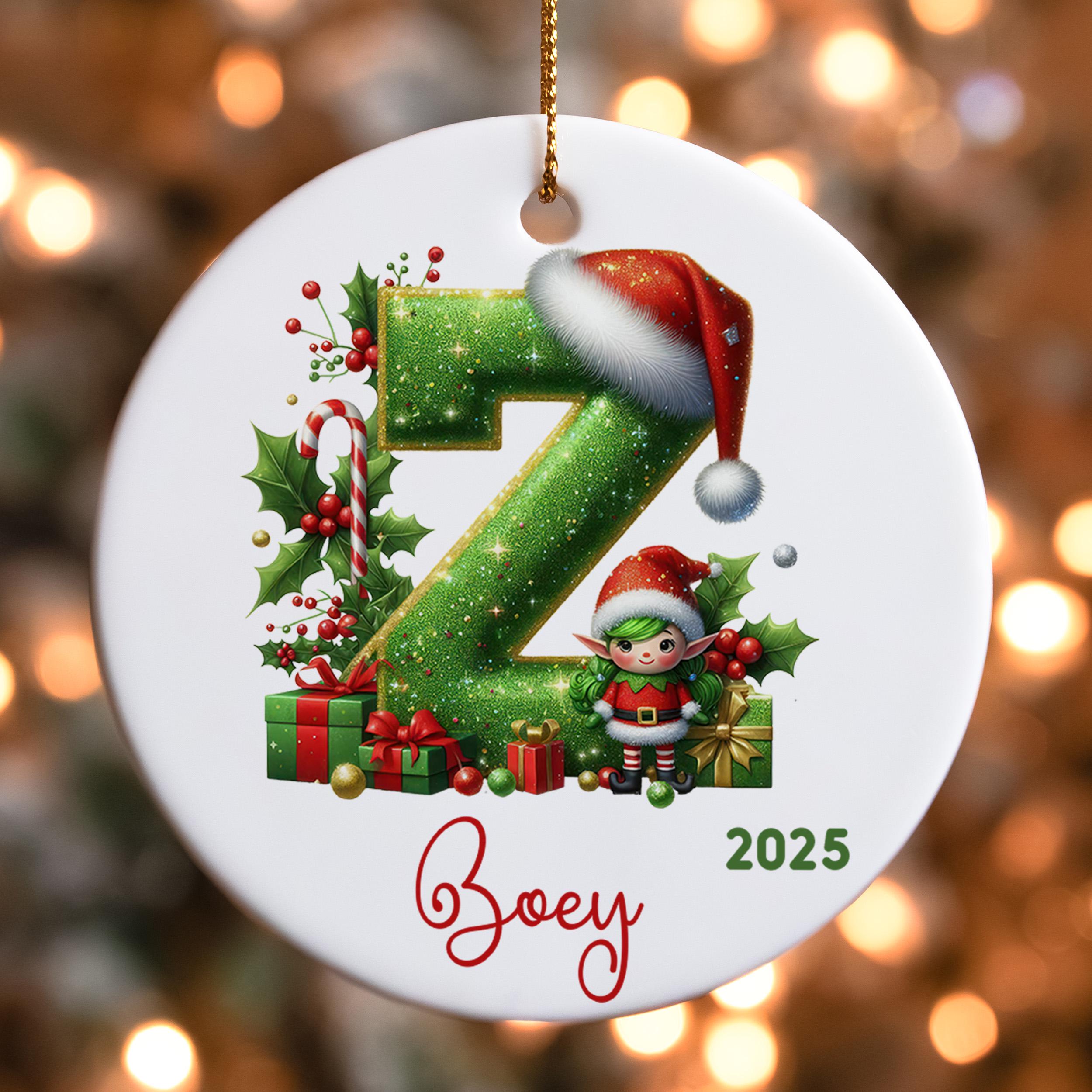 A white ornament with a green glittery letter "Z" and a small elf wearing a Santa hat, surrounded by Christmas decorations such as presents and holly leaves.