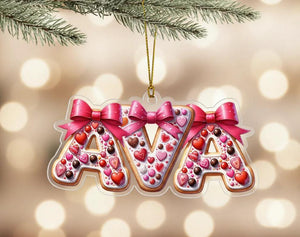 A clear ornament shaped like the letters "AVA" made of cookies, decorated with pink bows and hearts.