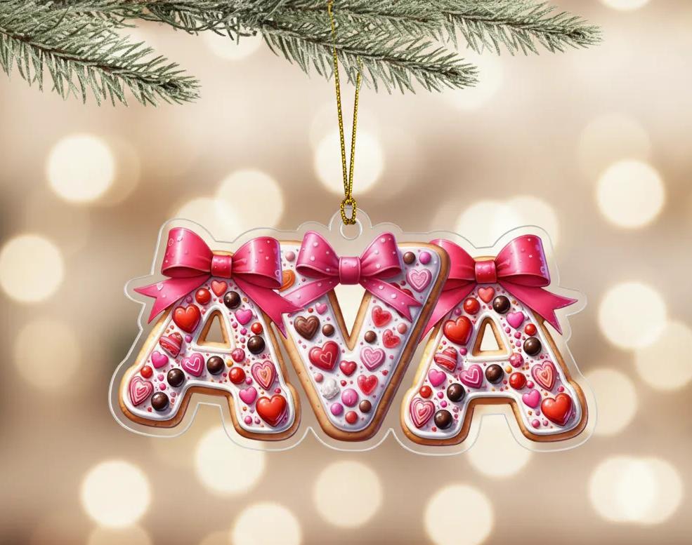 A clear ornament shaped like the letters "AVA" made of cookies, decorated with pink bows and hearts.