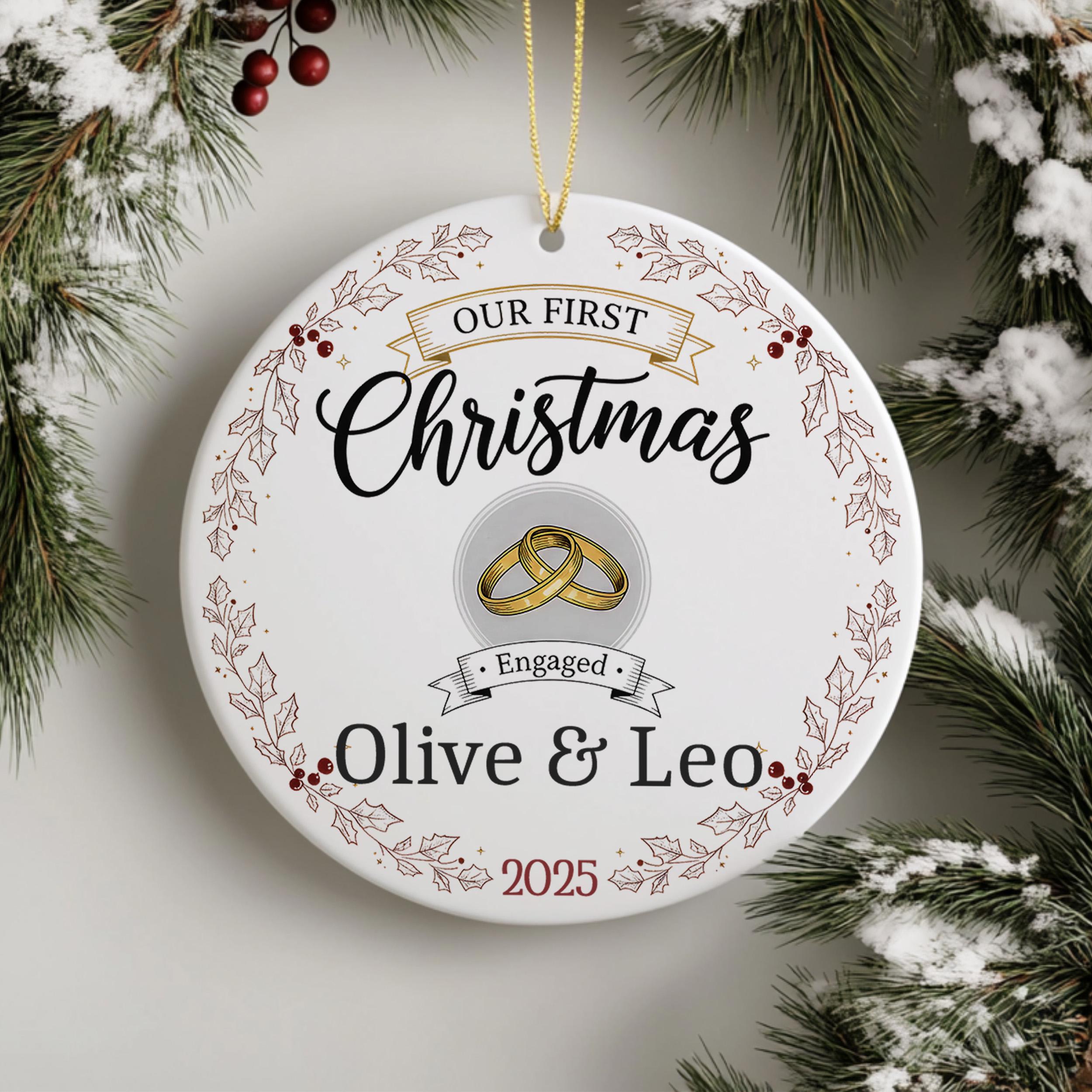 A white Christmas ornament with a gold ring and the text "Our first Christmas" and "Engaged Olive & Leo" printed on it, hanging on a pine tree branch.
