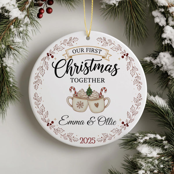 Personalised ceramic Christmas ornament featuring Our First Christmas Together text with two hot chocolate mugs, candy canes, Christmas tree, holly wreath border and custom names Emma & Ollie 2025 on festive background