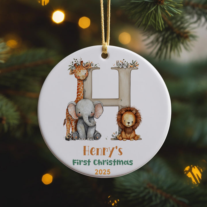 A white ornament with a letter &quot;H&quot; and illustrations of a giraffe, elephant, and lion, hanging on a Christmas tree.