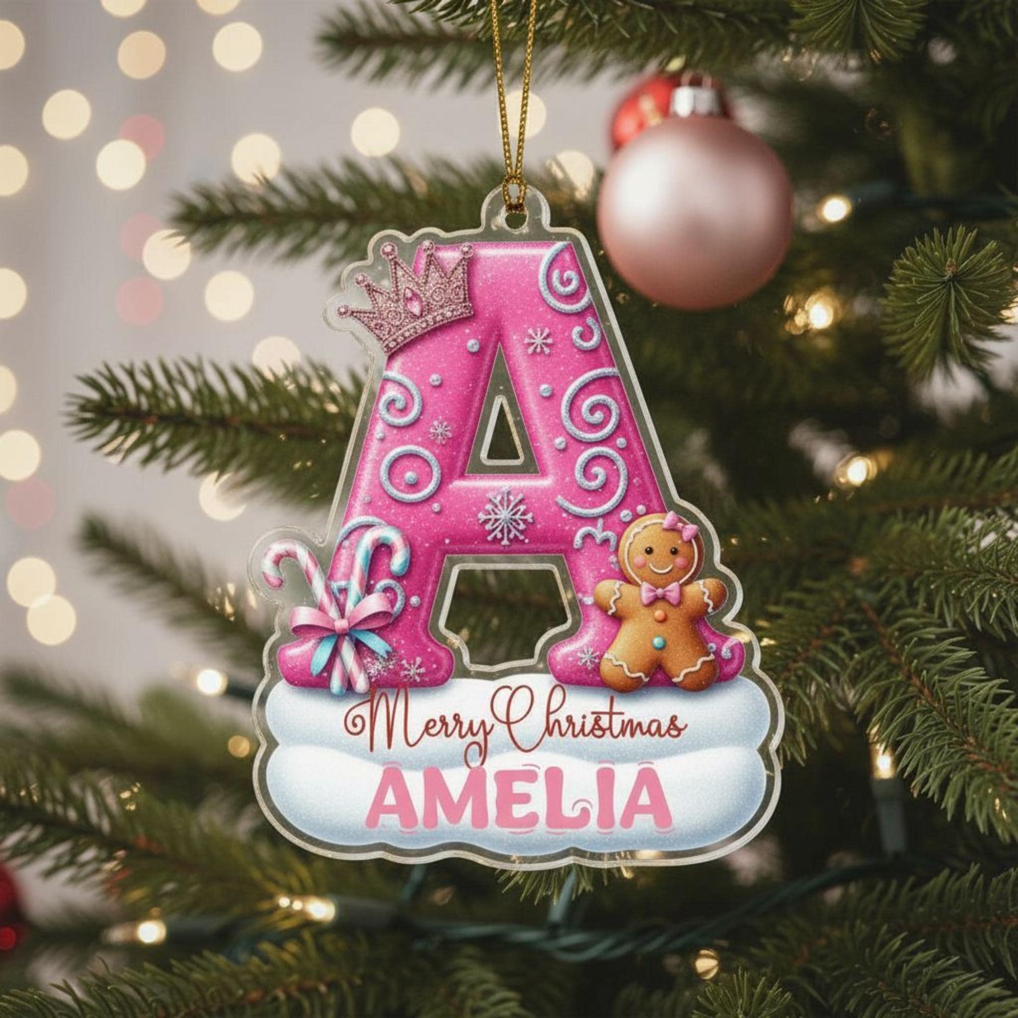 A pink ornament with a letter "A" and a gingerbread man is hanging on a Christmas tree.