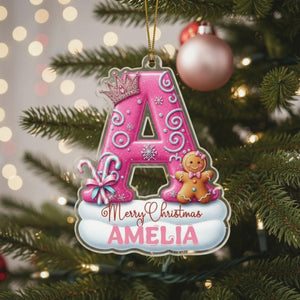 A pink ornament with a letter "A" and a gingerbread man is hanging on a Christmas tree.