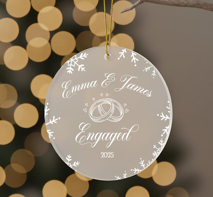 A clear ornament with a white design and text, hanging against a blurred background with bokeh lights.