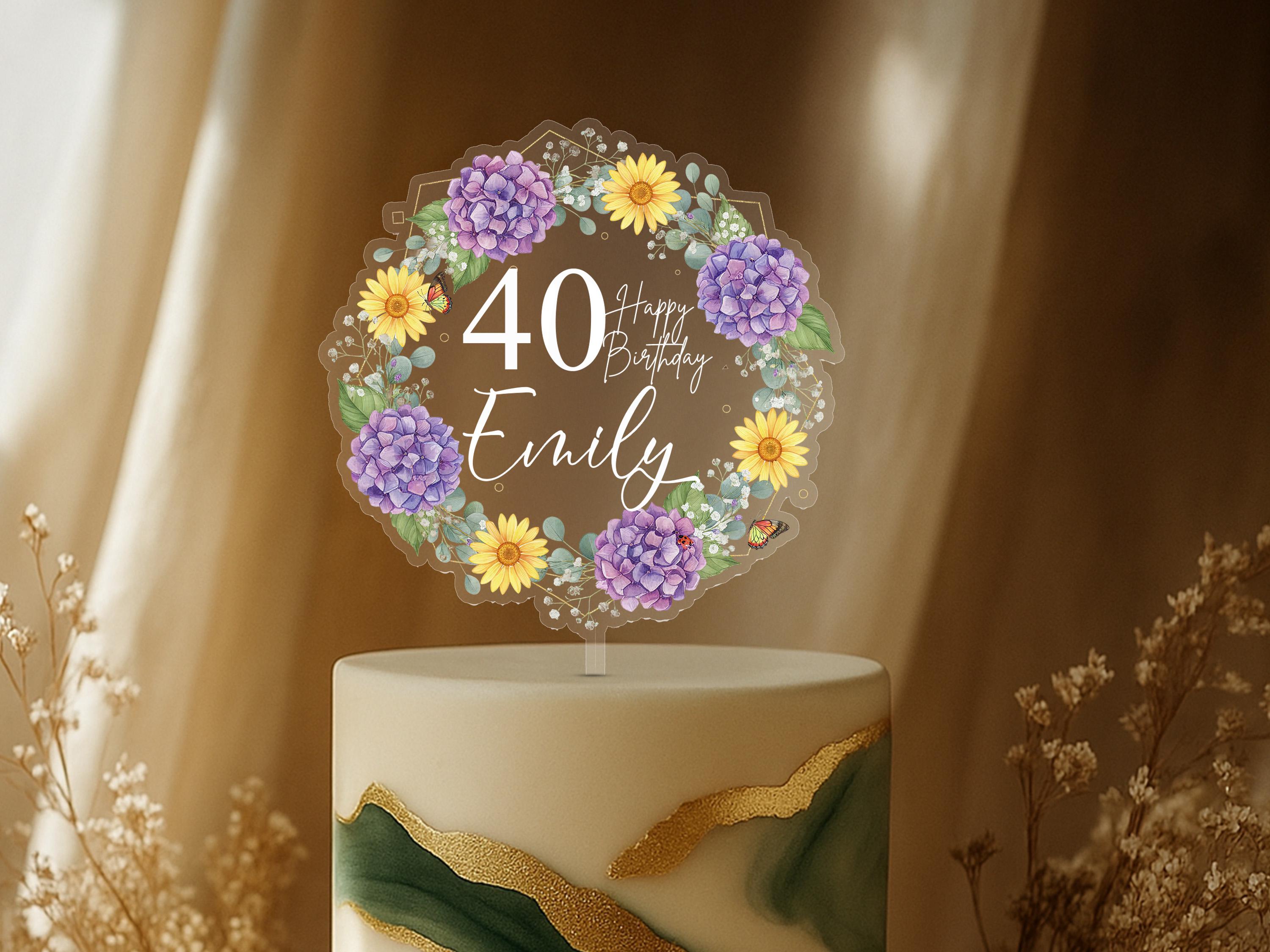 A birthday cake with a wreath-shaped topper that says "Happy Birthday Emily" surrounded by flowers and the number 40.