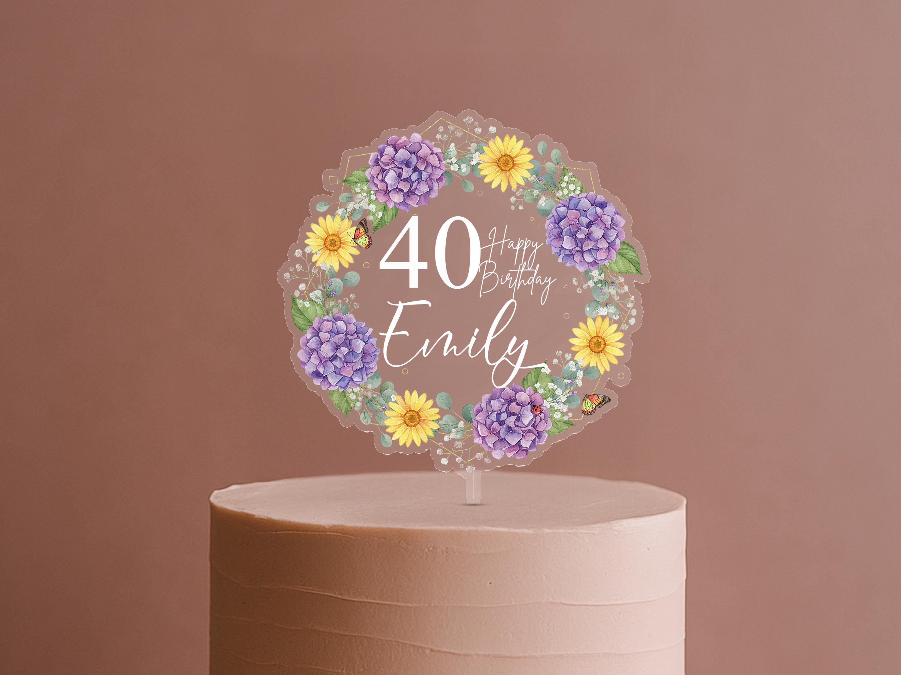 A cake topper with a wreath of purple and yellow flowers surrounding the number 40, along with the text "Happy Birthday Emily".