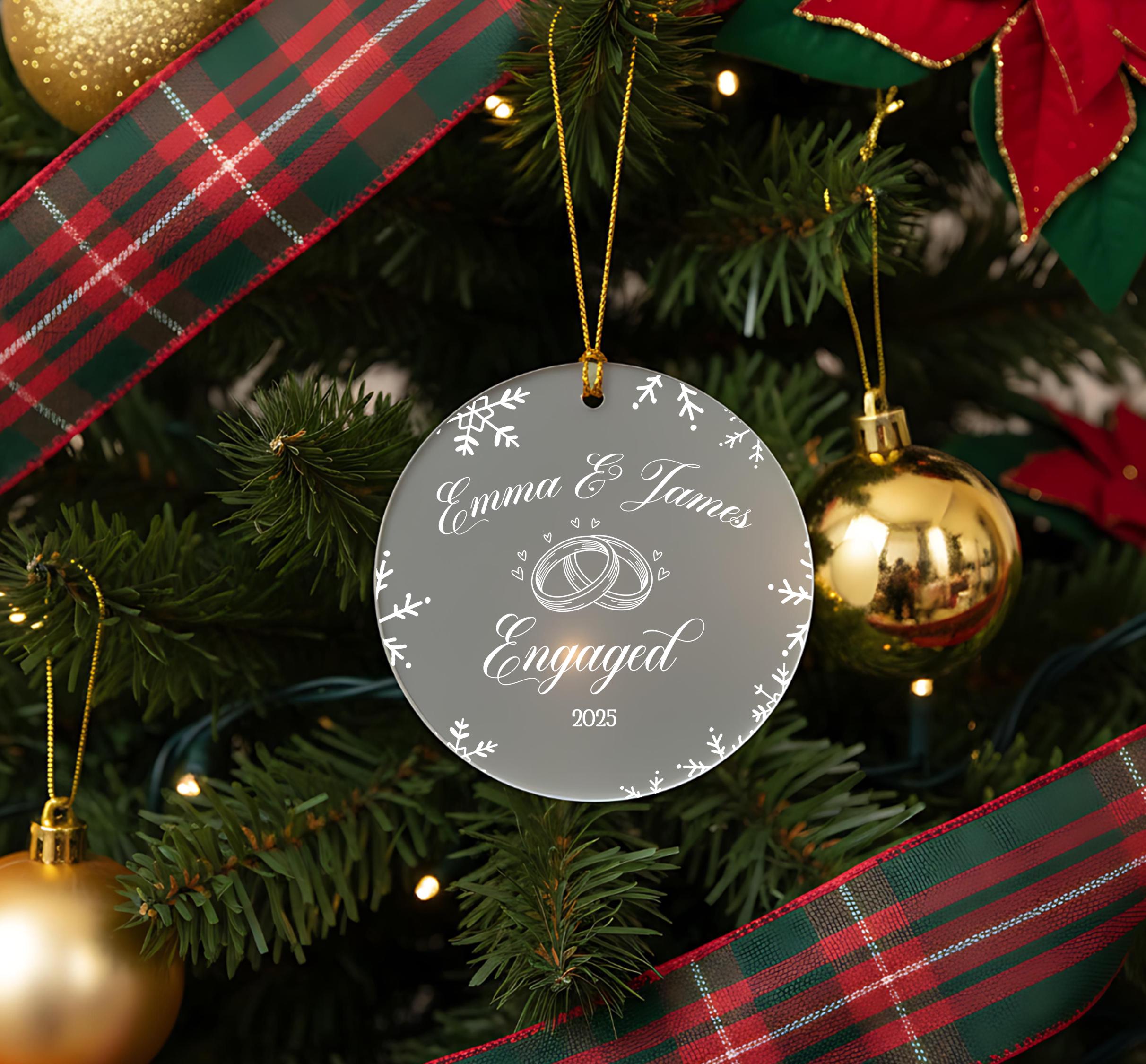 A Christmas tree decorated with ornaments, including a clear ornament with a wedding ring design and the text "Emma & James Engaged" on it.