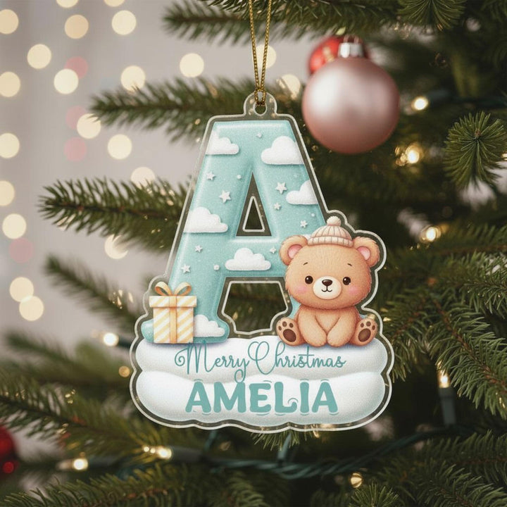 A Christmas ornament with a teddy bear and presents, hanging on a tree.