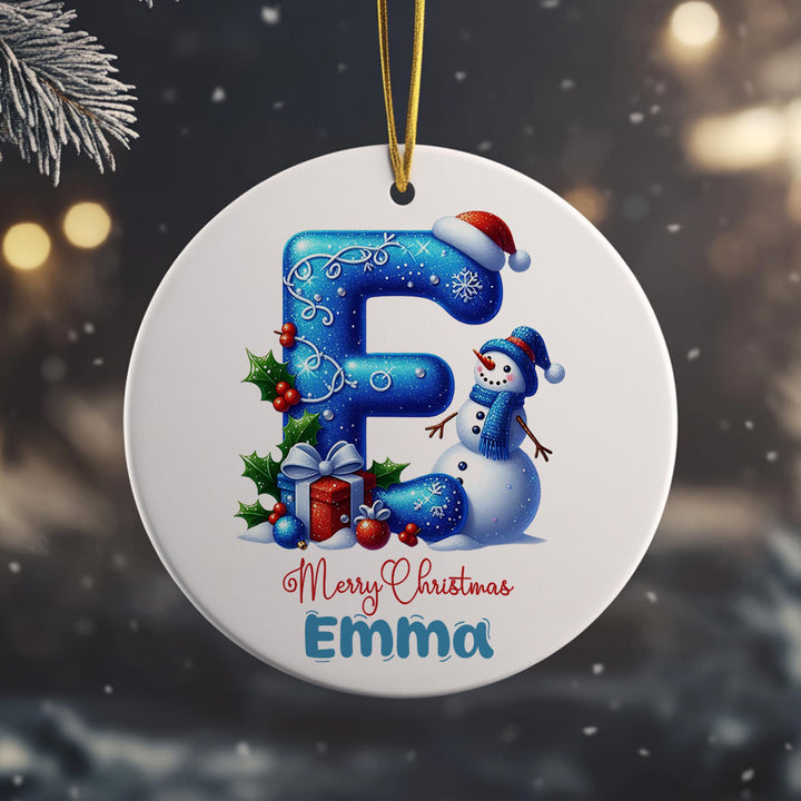 A round ornament with a snowman and Christmas decorations, including a letter &quot;F&quot; and the text &quot;Merry Christmas Emma&quot;.