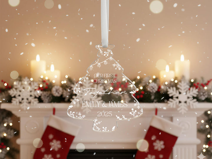 A Christmas ornament with the text &quot;Our first Christmas together&quot; and &quot;Together Emily & James 2020&quot; is displayed in front of a fireplace with lit candles and snowflakes.