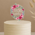 Personalised floral birthday cake topper featuring circular wreath of pink roses, daisies, eucalyptus and lavender, custom name Isabella with Happy Birthday 50 text, displayed on white frosted cake