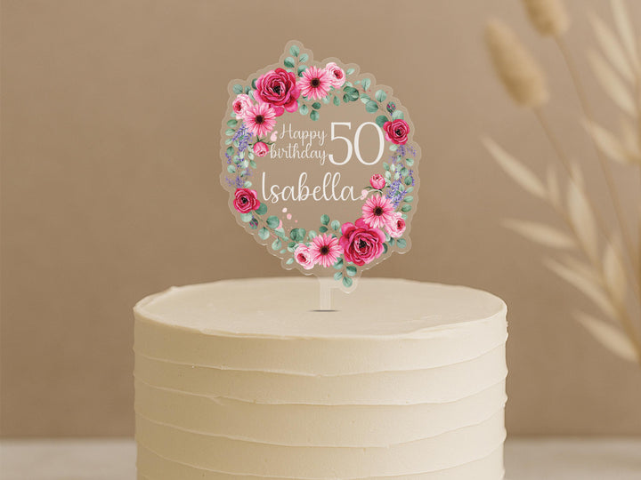 Personalised floral birthday cake topper featuring circular wreath of pink roses, daisies, eucalyptus and lavender, custom name Isabella with Happy Birthday 50 text, displayed on white frosted cake