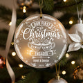 Personalised first Christmas engaged ornament hanging on Christmas tree showing frosted acrylic design with hot chocolate mugs, hearts, snowflakes and festive details, engraved with couple names Violet and George 2025, surrounded by bronze baubles and pine branches